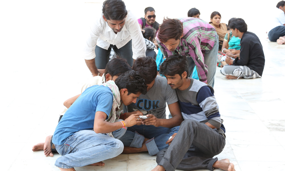 A group gathering around a man with his mobile phone
